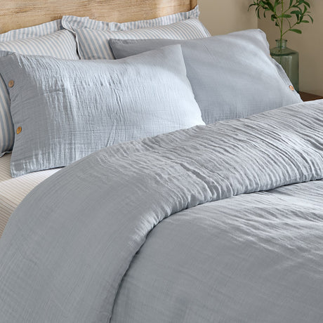 Lark Cotton Plain Duvet Cover Set in Mineral Blue on a bed, showing crinkled double-layer muslin cotton with a matching pillowcase and buttoned sham.