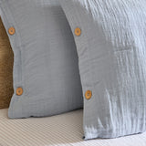 Close-up of the Lark Cotton Plain Duvet Cover Set in Mineral Blue, showing crinkled double-layer muslin fabric with wooden button fastenings on the pillowcase edge.