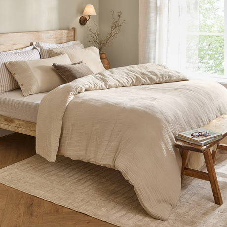Lark Cotton Plain Duvet Cover Set in Natural, crinkled muslin cotton bedding on a wooden bed with striped pillowcases, styled in a neutral bedroom setting.