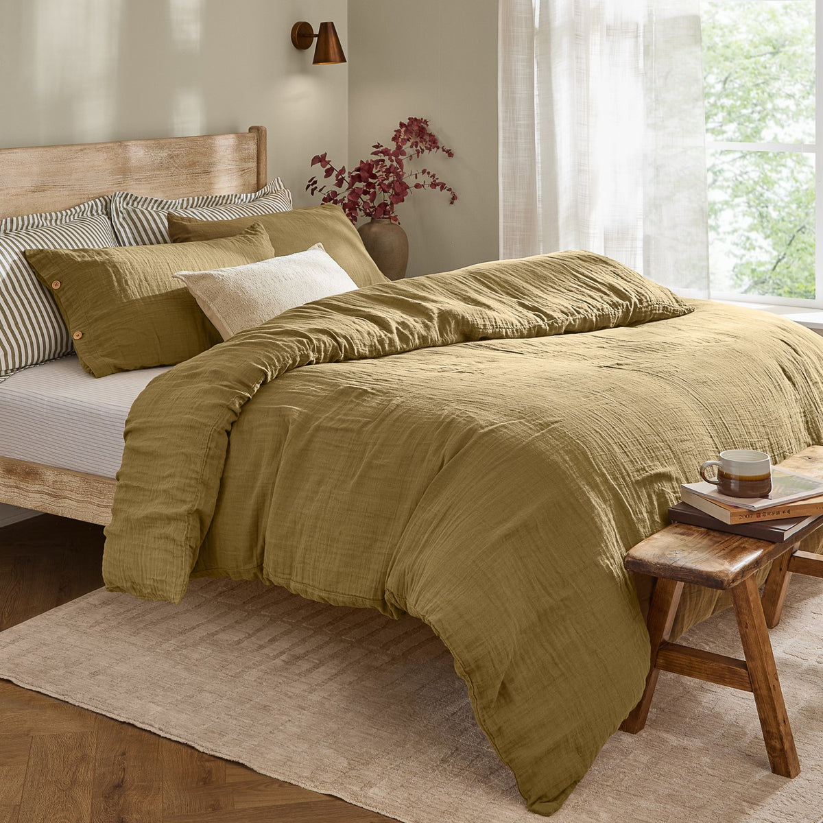 Lark Cotton Plain Duvet Cover Set in olive on a bed with crinkled muslin texture and wooden button-fastened pillowcases, shown in a bedroom with striped accent pillows.