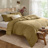 Lark Cotton Plain Duvet Cover Set in olive on a bed with crinkled muslin texture and wooden button-fastened pillowcases, shown in a bedroom with striped accent pillows.