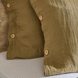 Close-up of the Lark Cotton Plain Duvet Cover Set in olive, showing crinkled muslin cotton pillowcases with wooden button fastenings on a striped bed base.