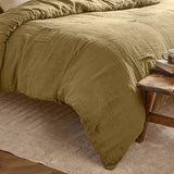 Lark Cotton Plain Duvet Cover Set in Olive, crinkled double-layer muslin cotton bedding on a bed, shown beside a wooden stool with books and a mug.