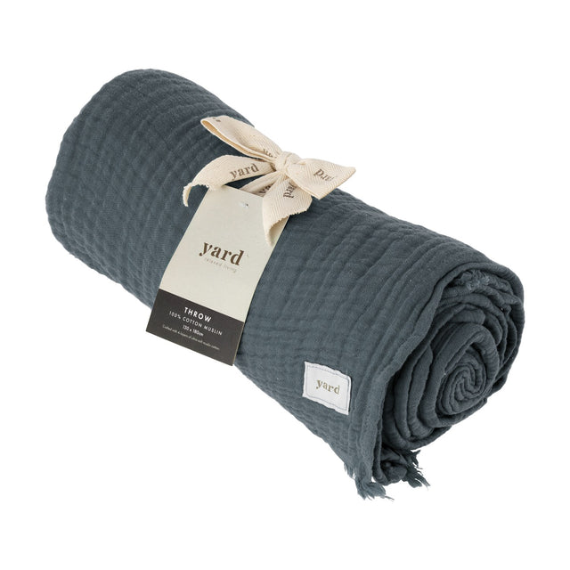 Lark Plain Cotton Throw in dusk blue, rolled up with frayed edge visible, textured cotton muslin fabric and cream branded tag tied with ribbon, shown on a plain white background.