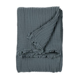 Lark Plain Cotton Throw in dusk blue, folded to show its crinkled cotton muslin texture and frayed edge, on a plain white background.