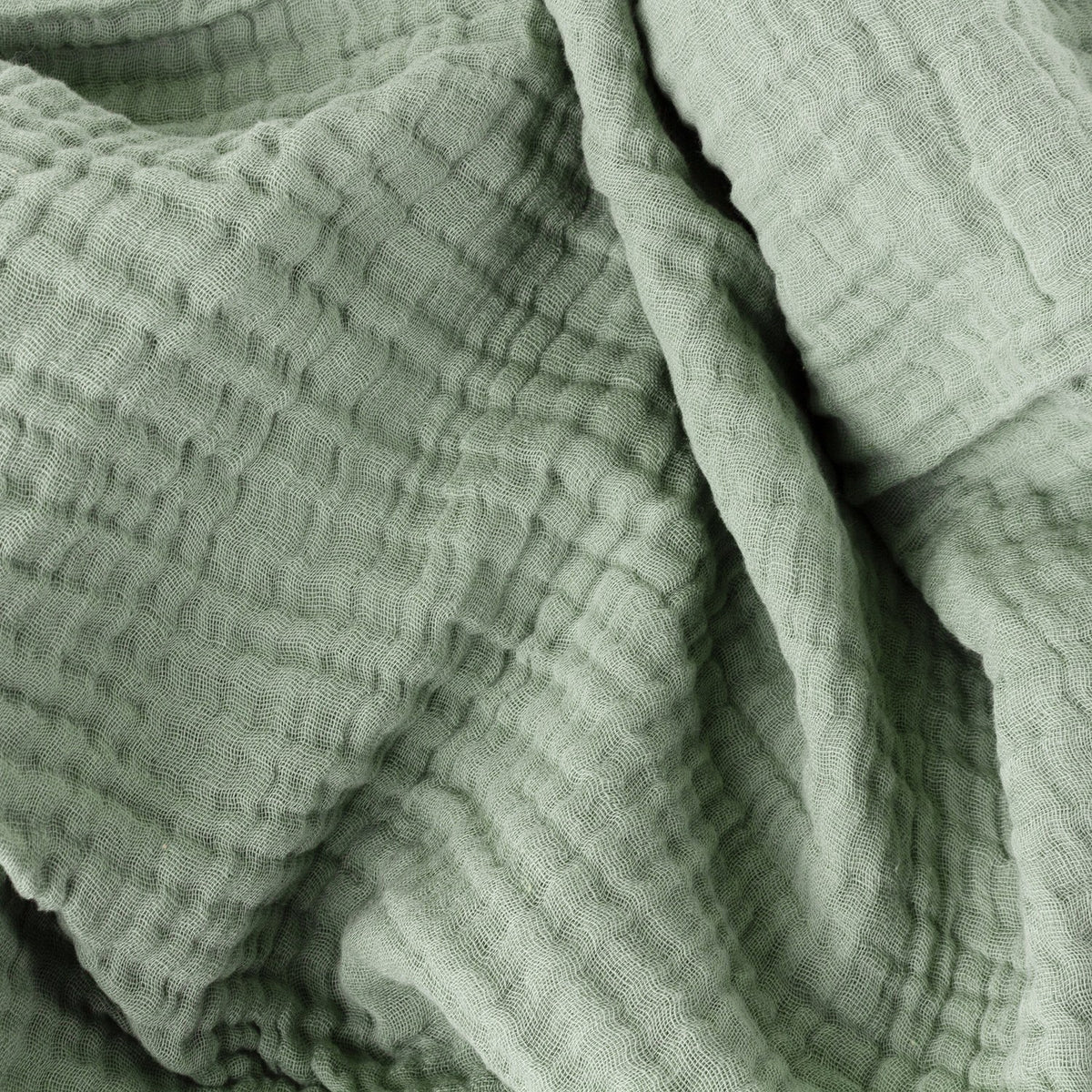 Close-up of the Lark Plain Cotton Throw in eucalyptus green, showing four-layer muslin cotton with a soft crinkled, waffled texture and folded drape.