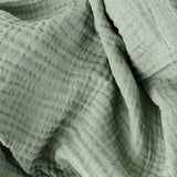 Close-up of the Lark Plain Cotton Throw in eucalyptus green, showing four-layer muslin cotton with a soft crinkled, waffled texture and folded drape.