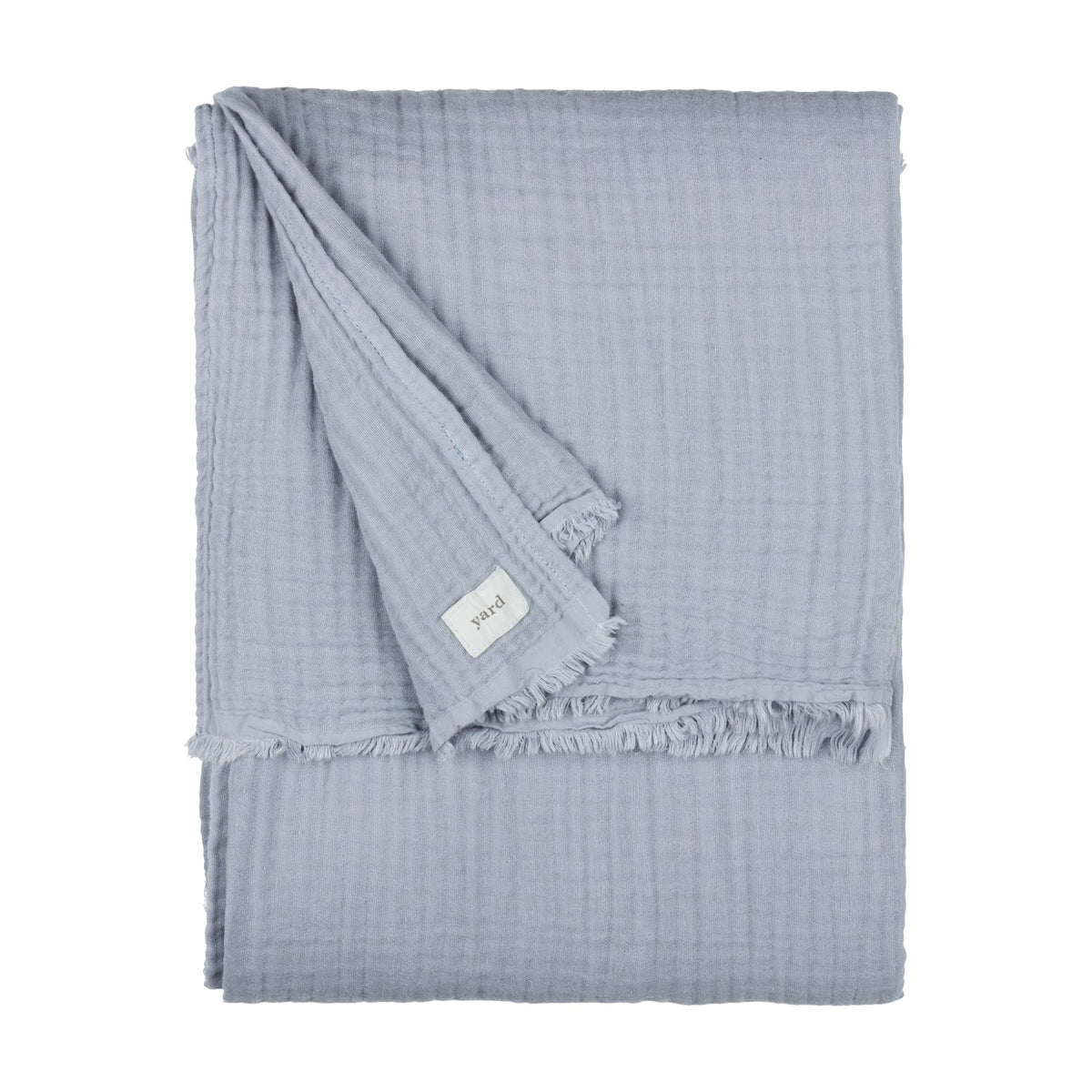 Lark Plain Cotton Throw in mineral blue, folded showing crinkled muslin texture and frayed edge with fabric label, on a plain white background.