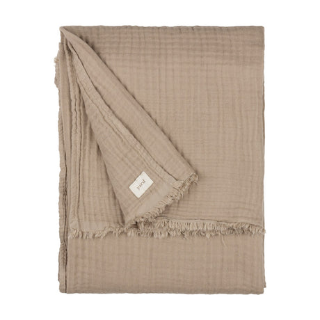 Lark Plain Cotton Throw in mole, a folded four-layer cotton muslin throw with a fringed edge and fabric brand tag, shown on a plain white background.