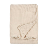 Lark Plain Cotton Throw in natural beige, folded to show its crinkled muslin texture and frayed edge detail against a plain white background.