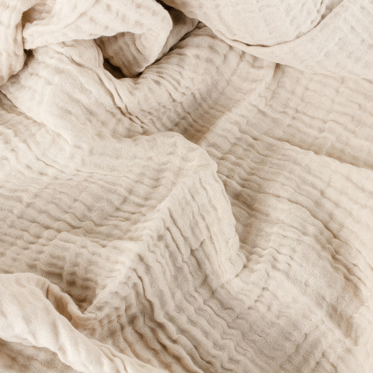 Close-up of the Lark Plain Cotton Throw in natural beige, showing the crinkled four-layer muslin texture in soft folds.