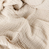 Close-up of the Lark Plain Cotton Throw in natural beige, showing the crinkled four-layer muslin texture in soft folds.