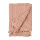 Lark Plain Cotton Throw in pink clay, folded to show crinkled muslin texture and fringed edge, on a plain white background.
