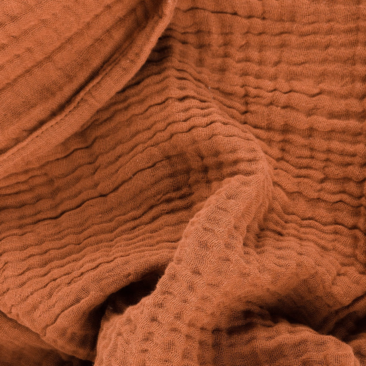 Lark Plain Cotton Throw in pecan, shown draped in folds with a crinkled muslin texture and soft frayed edge visible.