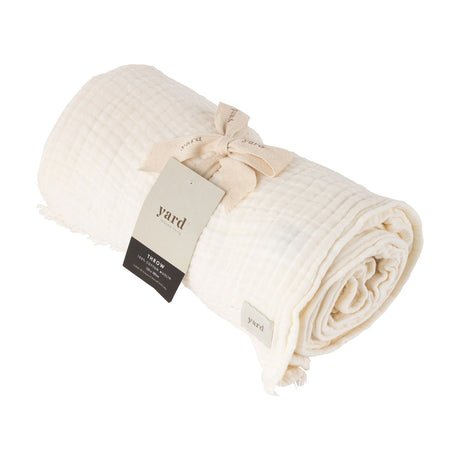 Lark Plain Cotton Throw in white, rolled and tied with a ribbon and branded tag, showing crinkled muslin texture and a frayed edge, on a plain white background.