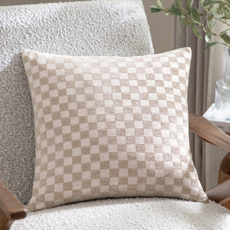 Larro Jacquard Chenille Cushion in Natural, showing a woven checkerboard pattern in beige and cream tones, styled on a bouclé armchair beside a wooden side table.