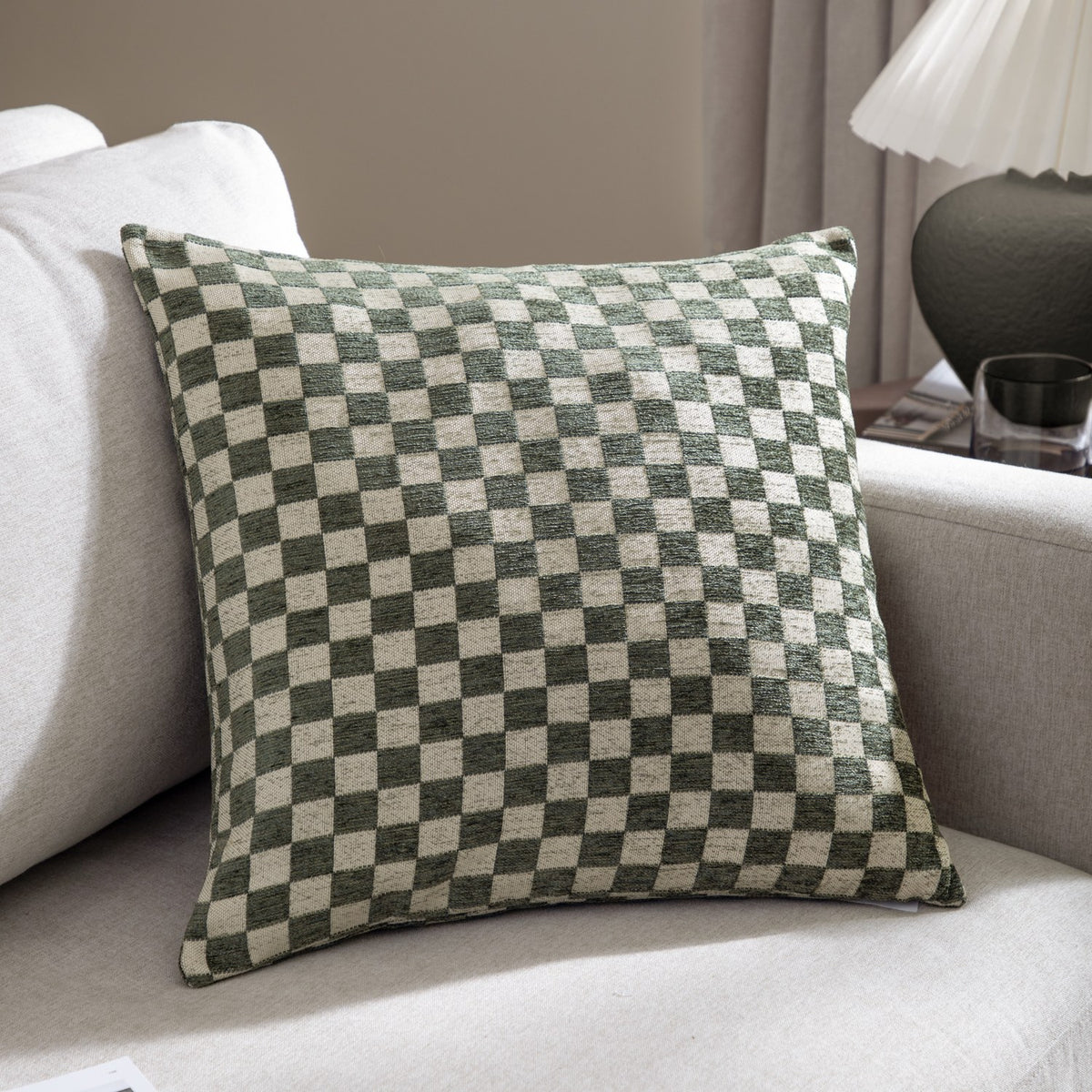 Larro Jacquard Chenille Cushion in Smoke Green, a square cushion with a checkerboard pattern in dusty green and natural chenille, shown on a light sofa.