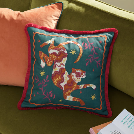 Les Animaux Tigeress square cushion in emerald green, embroidered tiger design in orange, rust and cream with red fringe trim, styled on a green sofa.