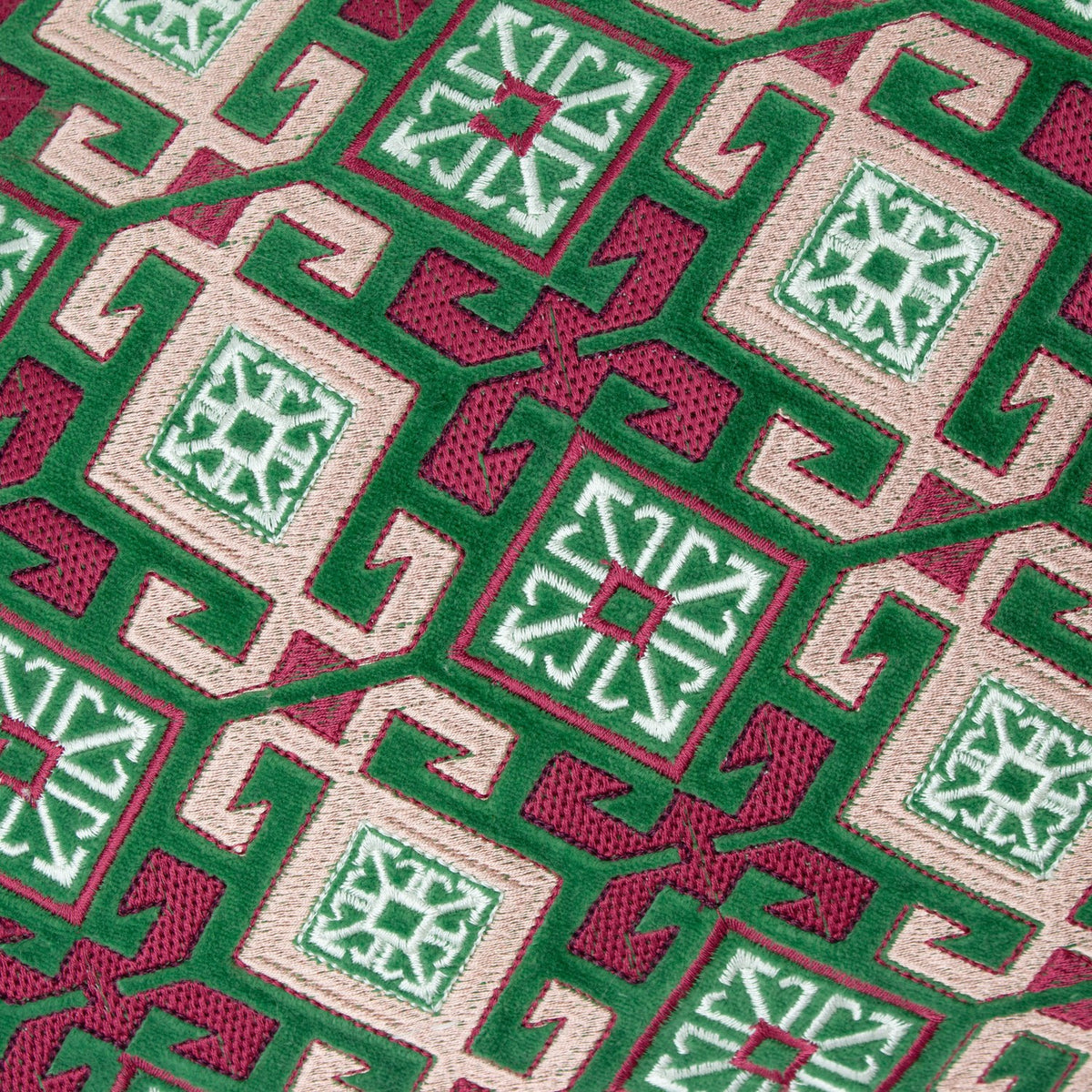 Close-up of the Laurel Velvet Cotton Cushion in cerise and jade, showing an embroidered geometric lattice pattern with diamond motifs in green, cream and pink threads on velvet.
