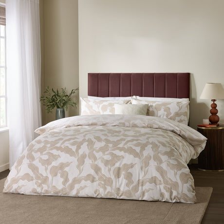 Lauro Reversible Leaf Duvet Cover Set in Stone, dressed on a bed with matching pillowcases in a bedroom with a maroon upholstered headboard and bedside lamp.