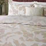 Lauro Reversible Leaf Duvet Cover Set in Stone, styled on a bed with matching pillowcases and cushions, showing a linear leaf print in soft tan and cream tones.