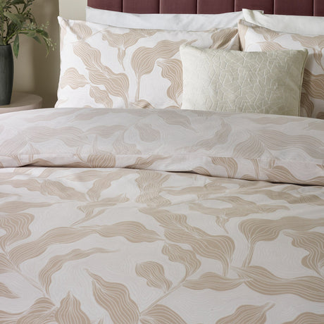 Lauro Reversible Leaf Duvet Cover Set in Stone, styled on a bed with matching pillowcases and cushions, showing a linear leaf print in soft tan and cream tones.