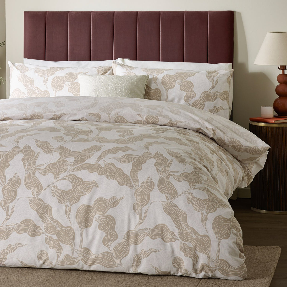 Lauro Reversible Leaf Duvet Cover Set in stone, styled on a bed with matching pillowcases in a bedroom with a burgundy upholstered headboard.