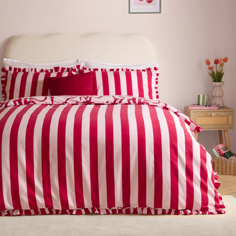 La Vie En Bows reversible duvet cover set in red and pink candy stripe on a bed with ruffled edges and matching pillowcases, styled in a bedroom with a cream headboard.