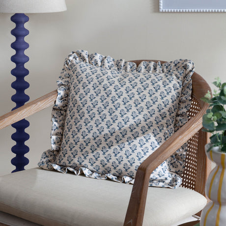 Lulah Block Floral Linen Cushion in blue and natural linen-blend fabric with ruffled edge, styled on a rattan-back chair in a living room setting.