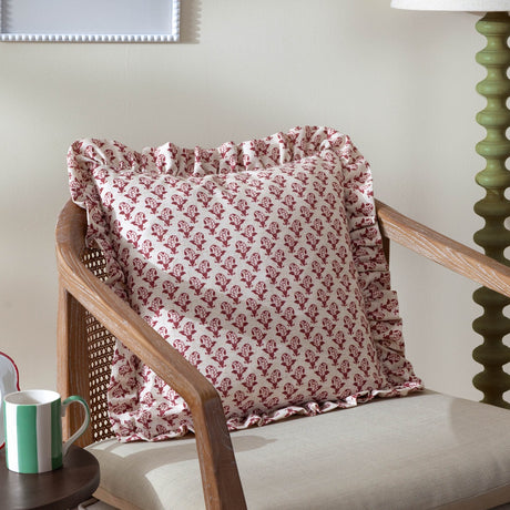 Lulah Block Floral Linen Cushion in red and natural with ruffled edge trim, styled on a rattan-armed wooden chair beside a green table lamp.