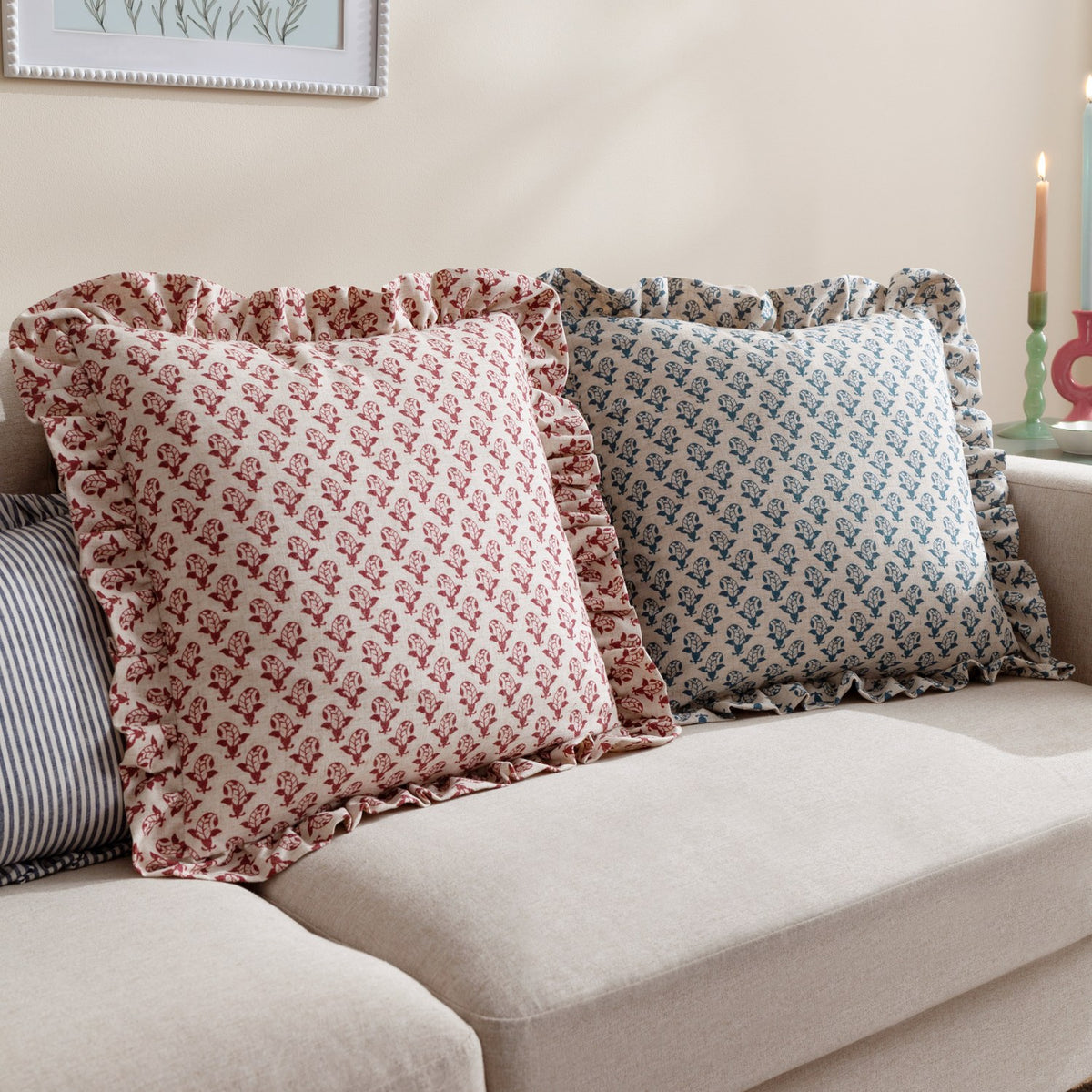 Lulah Block Floral Linen Cushion in red, square with ruffled edge trim, shown on a beige sofa beside a matching blue floral cushion.