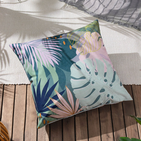 Square teal reversible polyester cushion with tropical palm leaf print in mint, pink and amber tones, shown outdoors on wooden decking.