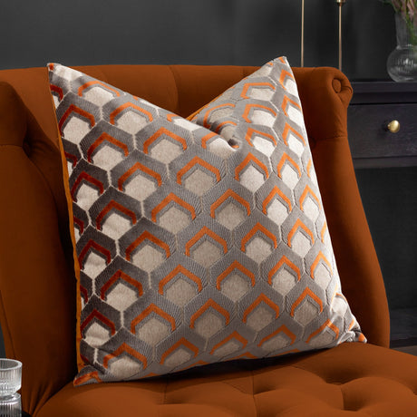 Ledbury Jacquard Velvet Cushion in ginger and grey with a raised geometric hexagon pattern, styled on a burnt orange armchair in a living room setting.