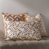 Ledbury Jacquard Velvet Cushion in Ginger/Grey, rectangular with diamond geometric pattern, styled with patterned cushions on a grey ottoman against a neutral wall.