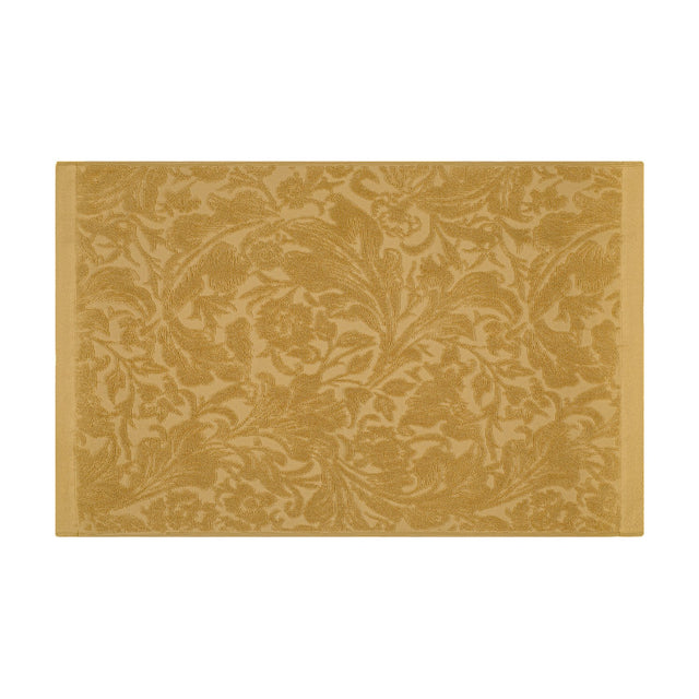 Leicester Floral Cotton Bath Mat in gold, rectangular with a woven scrolling floral pattern edge to edge and plain borders on the shorter sides, shown on a white background.