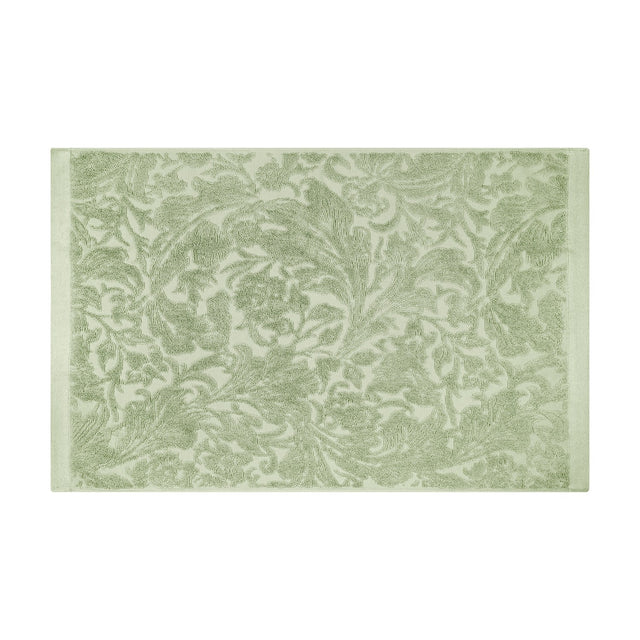 Leicester Floral Cotton Bath Mat in sage green with a raised scrolling acanthus leaf pattern and plain woven side borders, shown on a white background.
