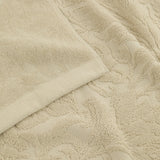 Close-up of a Leicester floral cotton towel in natural, showing folded plain-woven edge and a raised scrolling leaf and bloom pattern sculpted into the pile.