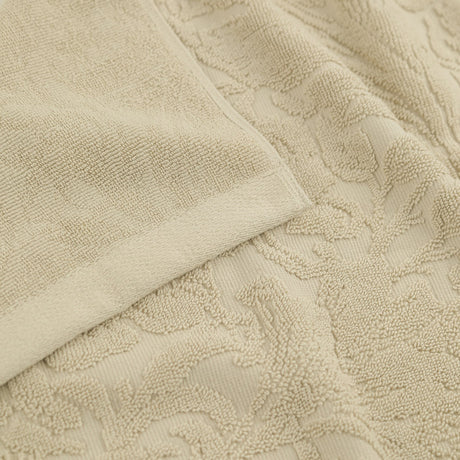 Close-up of a Leicester floral cotton towel in natural, showing folded plain-woven edge and a raised scrolling leaf and bloom pattern sculpted into the pile.