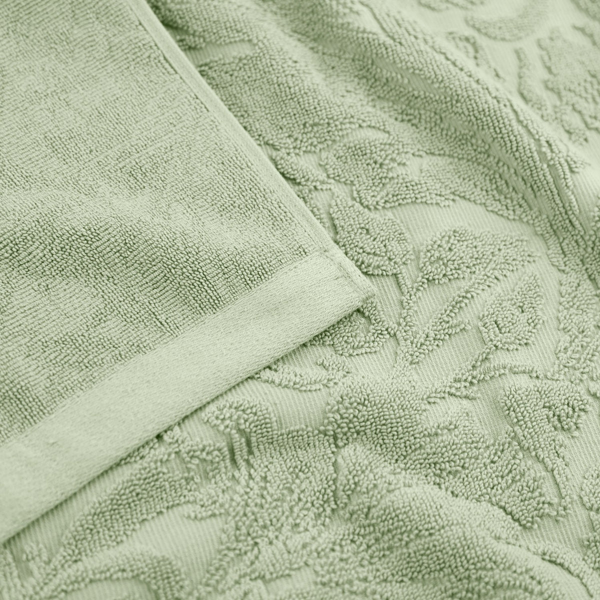 Close-up of Leicester Floral Cotton Towels in sage green, showing a raised leaf and foliage pattern woven into the cotton pile with a plain woven border edge.