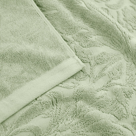 Close-up of Leicester Floral Cotton Towels in sage green, showing a raised leaf and foliage pattern woven into the cotton pile with a plain woven border edge.