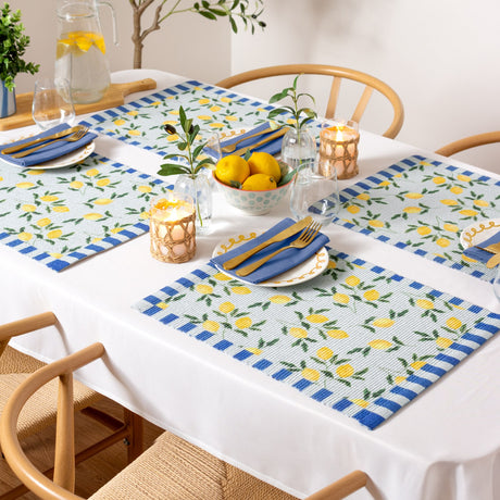Lemons Floral Polyester Placemats in blue set on a dining table with striped borders, yellow lemon and leaf print, styled with blue napkins, gold cutlery, candles, and a lemon centrepiece.