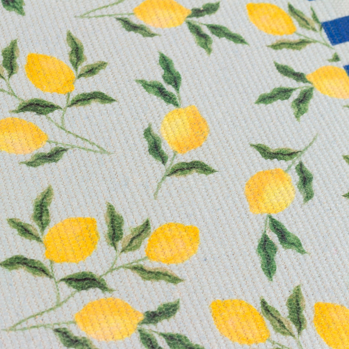 Close-up of a Lemons Floral Polyester Placemat showing yellow lemons and green leaves on a pale woven fabric, edged with a blue striped border.