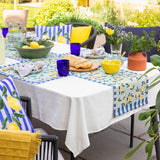 Lemons Floral Polyester Placemats in blue used as a table runner on an outdoor dining table, featuring yellow lemon and green leaf prints bordered by blue stripes.