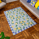 Lemons Striped Polyester Rug in blue, featuring a yellow lemon and leaf pattern on a pale blue ground with a blue and cream block border, shown on a wooden deck beside outdoor sofa cushions.