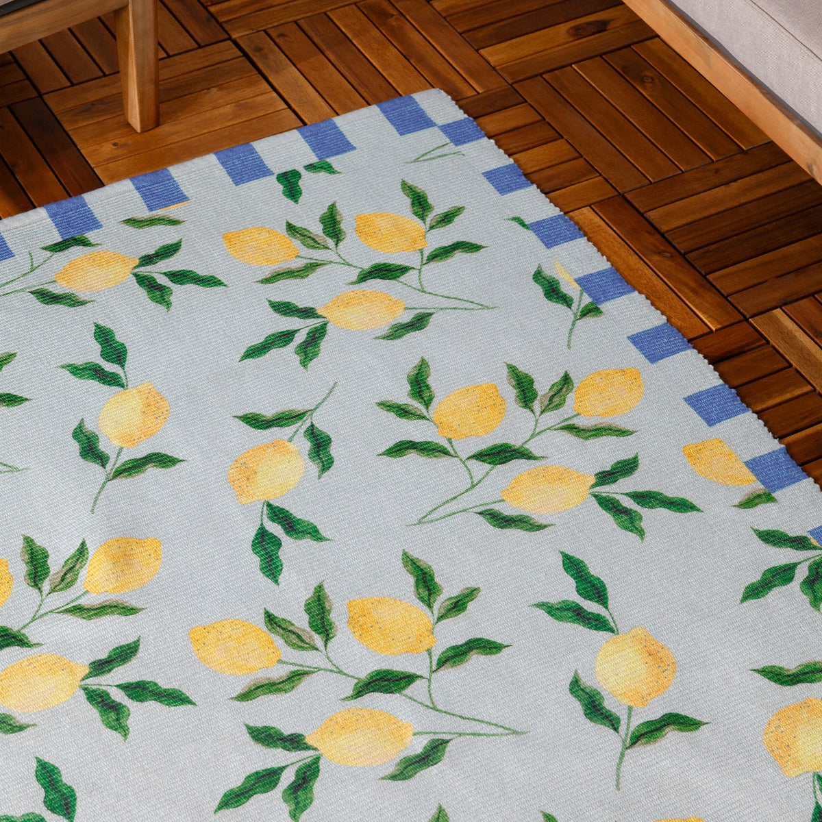 Lemons Striped Polyester Rug in blue with yellow lemon and green leaf print, bordered by a blue and cream block stripe, shown on a wooden floor.