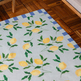 Lemons Striped Polyester Rug in blue with yellow lemon and green leaf print, bordered by a blue and cream block stripe, shown on a wooden floor.