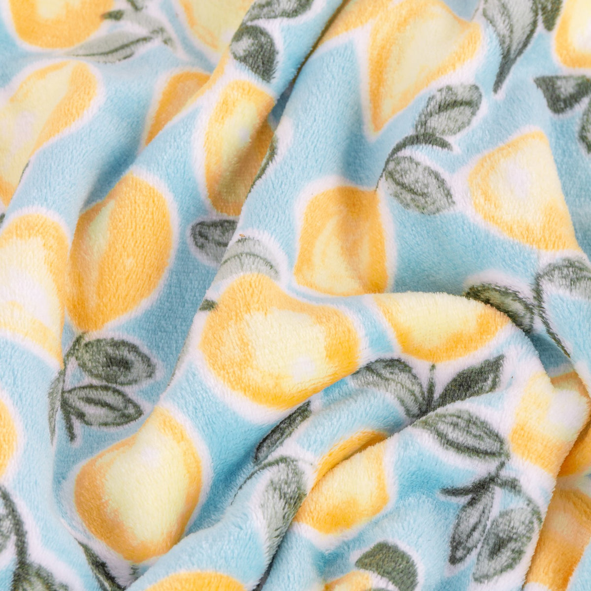 Close-up of the Lemons Printed Polyester Throw in blue, showing folded fleece fabric with a repeated yellow lemon and grey-green leaf print on a pale blue ground.