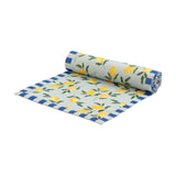 Lemons Floral Polyester Table Runner in blue, partially rolled to show a pale woven ground with yellow lemon clusters, green foliage, and a blue striped border, on a white background.