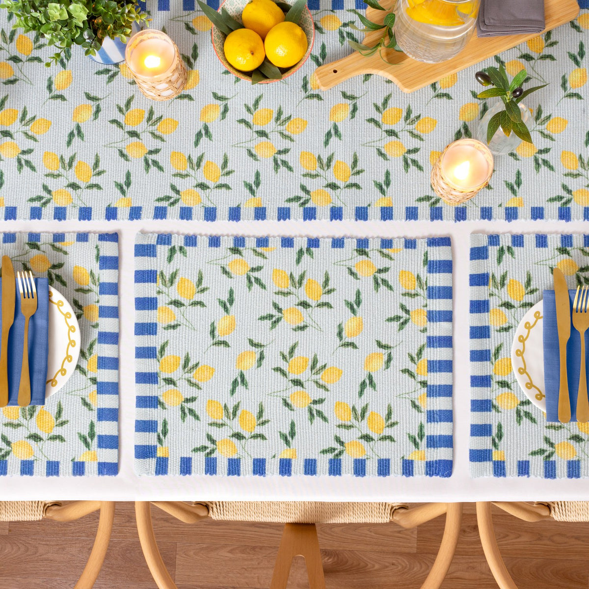 Lemons Floral Polyester Table Runner in blue, shown on a dining table with matching striped placemats, yellow lemon print, and blue and white striped borders.