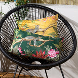 Rectangular Leopard Jungle polyester cushion in forest green with a leopard on a branch, tropical foliage and pink peonies, shown on a black woven chair beside a matching mustard-yellow cushion.